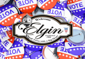Welcome sign for Elgin over a background of red, white, and blue VOTE buttons, highlighting the upcoming town of Elgin council election.