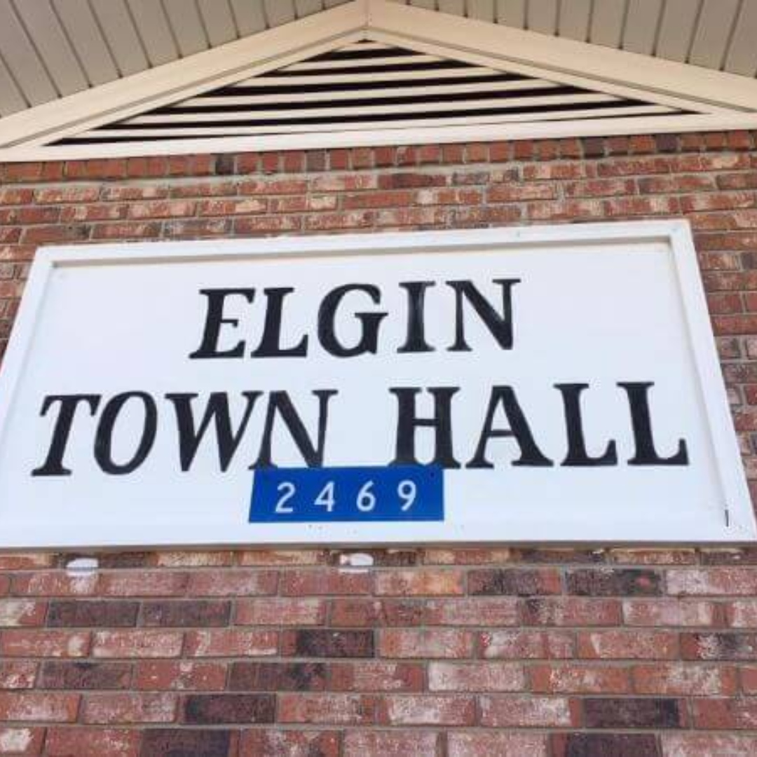 Sign reading Elgin Town Hall with address number 2469 on a brick wall, the headquarters for various Elgin departments and services.