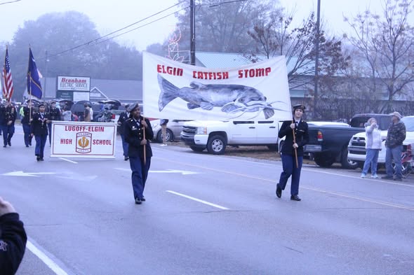 Marching band in a parade with Elgin Catfish Stomp and Lugoff-Elgin High School banners on a foggy day.